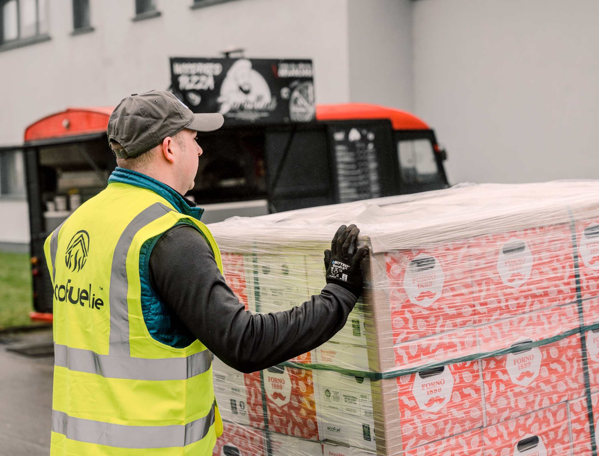 ECOFUEL™ delivery team in a high-visibility vest delivering a pallet of Forno1889 pizza logs in front of a Bartollini pizza truck in Galway, Ireland.